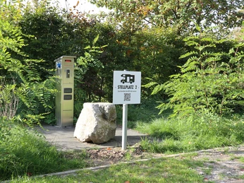 Versorgungsstation Stellplatz für Wohnmobile mit elektrischem Anschluss, umgeben von grünen Büschen und Bäumen.