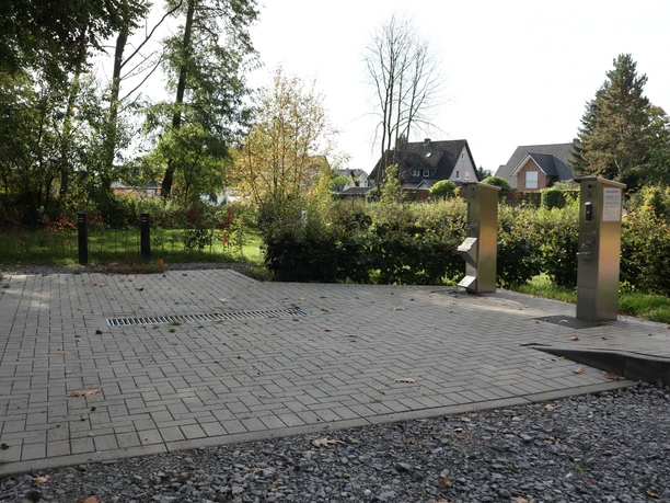 Wohnmobil-Entsorgungsstation mit zwei silbernen Säulen auf gepflastertem Bereich, umgeben von Bäumen.