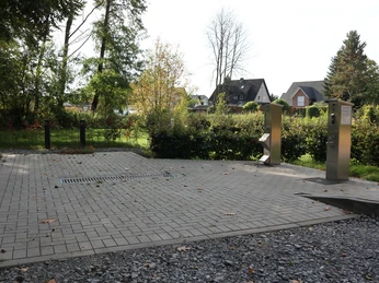 Ver- und Entsorgungsplatz Wohnmobil-Entsorgungsstation mit zwei silbernen Säulen auf gepflastertem Bereich, umgeben von Bäumen.