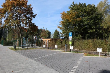 Parkplatz mit zwei ausgewiesenen Behindertenparkplätzen, umgeben von Bäumen in herbstlichen Farben.