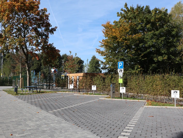 Parkplatz mit zwei ausgewiesenen Behindertenparkplätzen, umgeben von Bäumen in herbstlichen Farben.