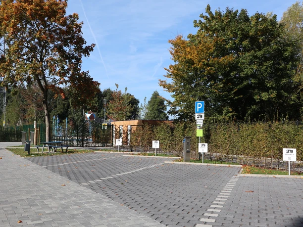 Stellplätze am Freibad Parkplatz mit zwei ausgewiesenen Behindertenparkplätzen, umgeben von Bäumen in herbstlichen Farben.