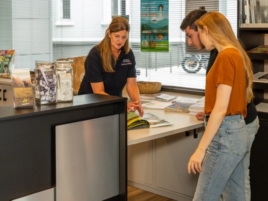 Tourist-Information am Deutschen Schloss- und Beschlägemuseum in Velbert Ein Mitarbeiter erklärt zwei jungen Besuchern an einem Tisch Informationsbroschüren in einem modernen Büro.