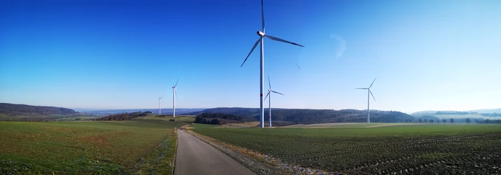 Windräder auf der Hüwe Windräder auf grünen Hügeln unter klarem Himmel, mit einem asphaltierten Weg im Vordergrund.