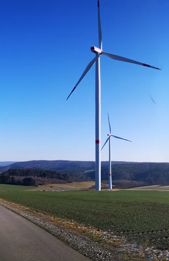 Windräder auf der Hüwe Windräder auf grünen Hügeln unter klarem Himmel, mit einem asphaltierten Weg im Vordergrund.