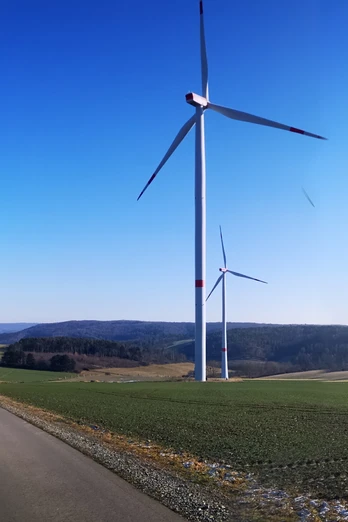 Windräder auf der Hüwe Windräder auf grünen Hügeln unter klarem Himmel, mit einem asphaltierten Weg im Vordergrund.