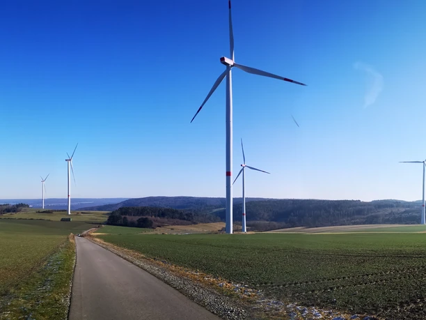 Windräder auf der Hüwe Windräder auf grünen Hügeln unter klarem Himmel, mit einem asphaltierten Weg im Vordergrund.