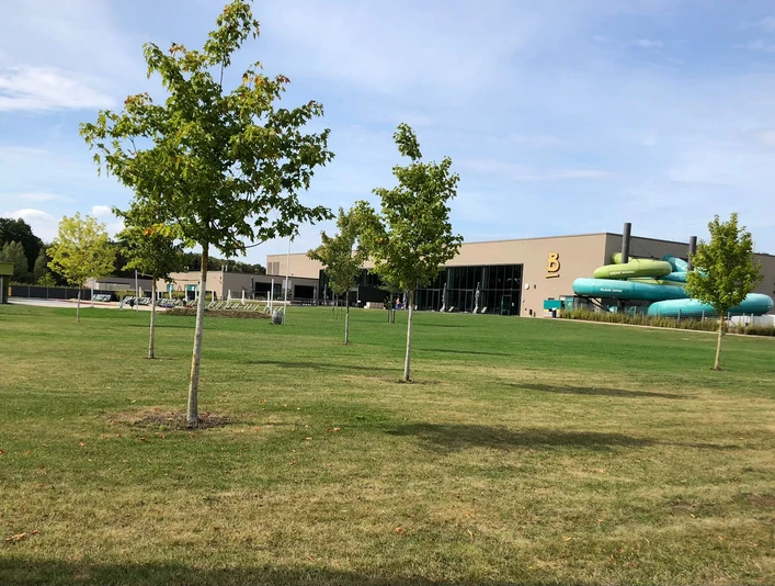 Ein modernes Freizeitbad mit großer grüner Liegewiese und blauer Rutsche im Hintergrund.
