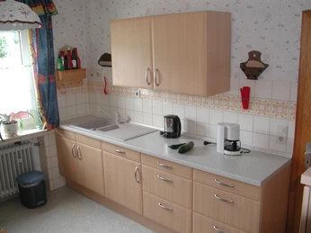 Helle Küche mit Holzschränken, Spüle, Kaffeemaschine, Fliesenrückwand und kleinem Fenster.