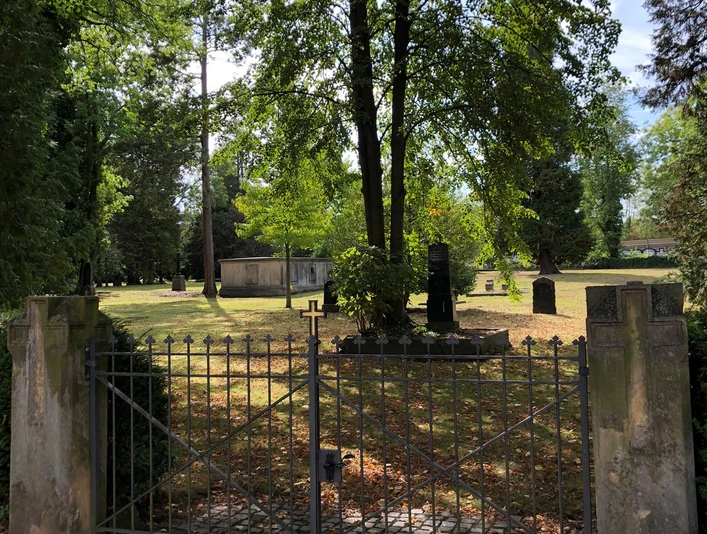 Alter Friedhof Neustadt Eingezäunter Friedhof umgeben von hohen Bäumen; Grabsteine verstreut, herbstliches Laub auf dem Boden.