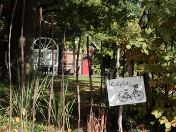Fahrradparkplatz Ein Parkplatzschild mit einem Fahrradmotiv, umgeben von üppiger, grüner Vegetation und Herbstlaub.