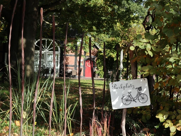Fahrradparkplatz Ein Parkplatzschild mit einem Fahrradmotiv, umgeben von üppiger, grüner Vegetation und Herbstlaub.