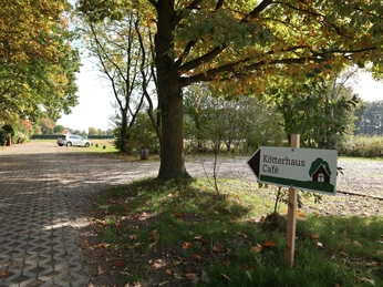 Parkplatz Kleiner Parkplatz unter Bäumen; Wegweiser zeigt Richtung Kötterhaus Café im idyllischen, ländlichen Gebiet.