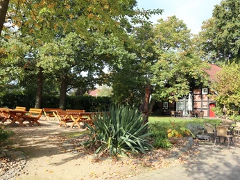 Biergarten Ein idyllischer Biergarten mit Holztischen und Stühlen im Schatten großer, grüner Bäume.