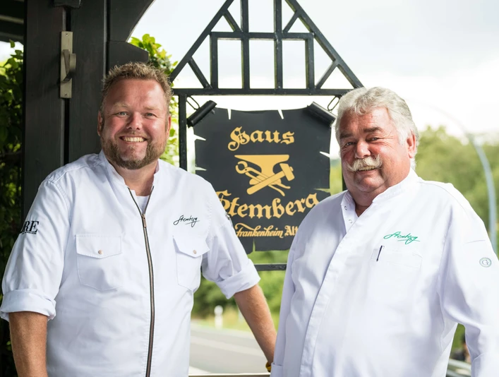 Sterneküche Haus Stemberg in Velbert Zwei Köche in weißer Kleidung stehen vor einem Schild des renommierten Haus Stemberg in Velbert.
