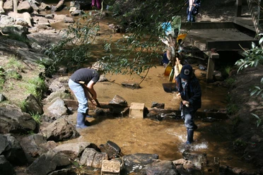 Bau eines Staudammes auf dem Abenteuerspielplatz Hilden Kinder spielen am Bachlauf und errichten einen kleinen Staudamm mit Steinen auf einem Abenteuerspielplatz.