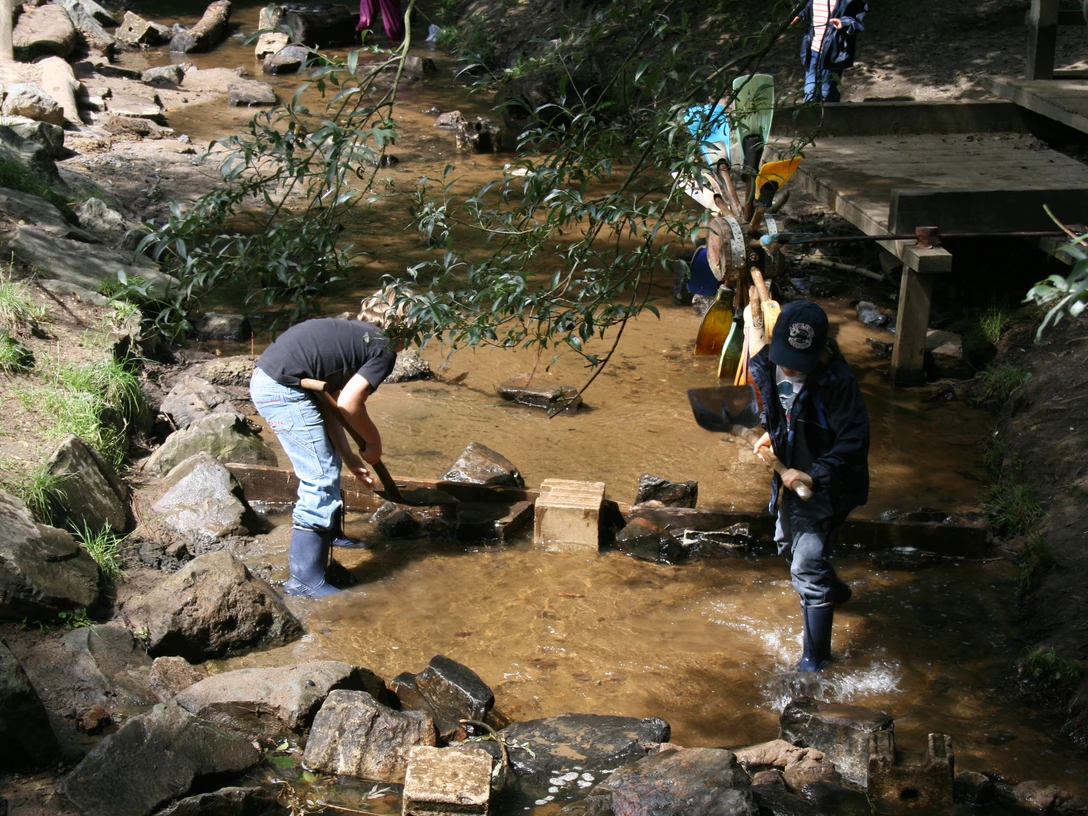 Bau eines Staudammes auf dem Abenteuerspielplatz Hilden Kinder spielen am Bachlauf und errichten einen kleinen Staudamm mit Steinen auf einem Abenteuerspielplatz.