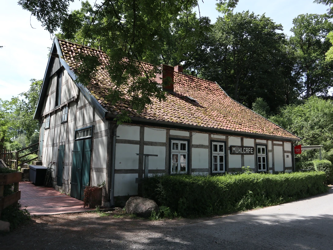 502B3A35-C8D4-4E78-8E1C-BA2390218E7E.jpeg Ein traditionelles Fachwerkhaus mit Ziegeldach, umgeben von Bäumen, steht am ruhigen Straßenrand.