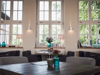 Helles, einladendes Café-Interieur mit großen Fenstern, gemütlichen Sitzplätzen und stilvoller Dekoration.