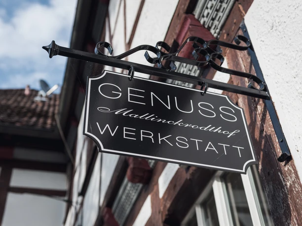 Genusswerkstatt exterior Schild der "Genusswerkstatt Mallinckrodthof", angebracht an einer Fachwerkfassade, zeigt den Namen.