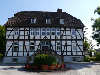 Historisches Fachwerkhaus mit symmetrischer Fensteranordnung, steinerner Treppe und blühendem Vorgarten.