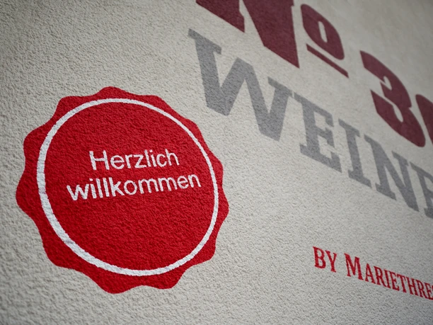 Rote Kreisgrafik mit "Herzlich willkommen" neben dem Schriftzug No 36 Weinbar an der Wand.