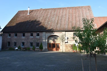 Ferienhaus an Vodes-Mühle Altes Backsteingebäude mit hohem Giebel und Rundbogentor, umgeben von einem gepflasterten Hof.