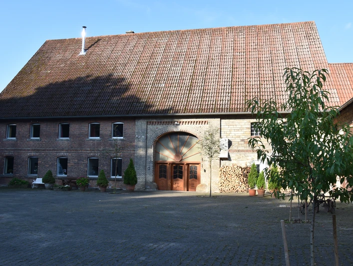 Ferienhaus an Vodes-Mühle Altes Backsteingebäude mit hohem Giebel und Rundbogentor, umgeben von einem gepflasterten Hof.