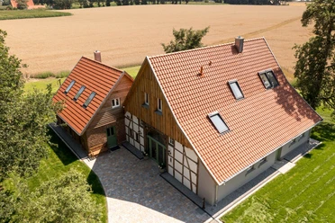 Zum Heuerling.jpg Zwei Fachwerkhäuser mit roten Dächern, umgeben von grünen Bäumen und einem goldenen Weizenfeld.