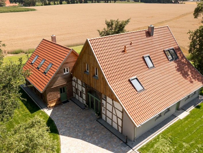 Zum Heuerling.jpg Zwei Fachwerkhäuser mit roten Dächern, umgeben von grünen Bäumen und einem goldenen Weizenfeld.