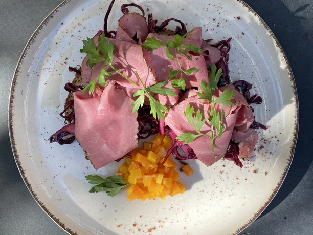 Ein Teller mit rosa Roastbeef, Rotkraut und gelben Würfeln, dekoriert mit frischen Petersilienblättern.