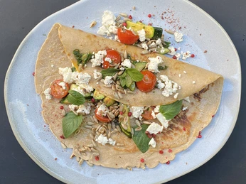 Zwei gefaltete Buchweizen-Crêpes, gefüllt mit Ziegenkäse, Kirschtomaten, Zucchini und Babyspinat.