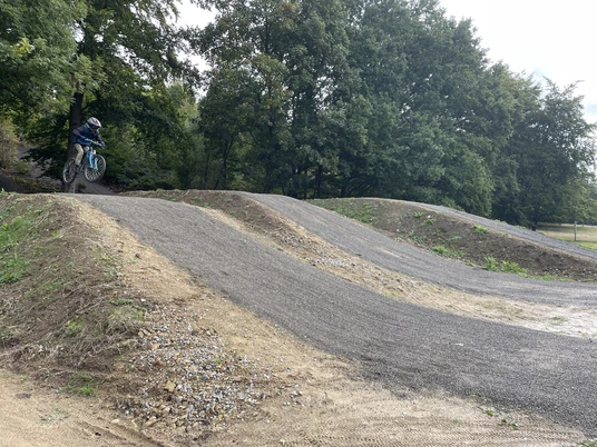 Bikepark Bad Wünnenberg Ein Mountainbiker springt über einen Hügel im Bikepark mit dicht bewaldetem Hintergrund.