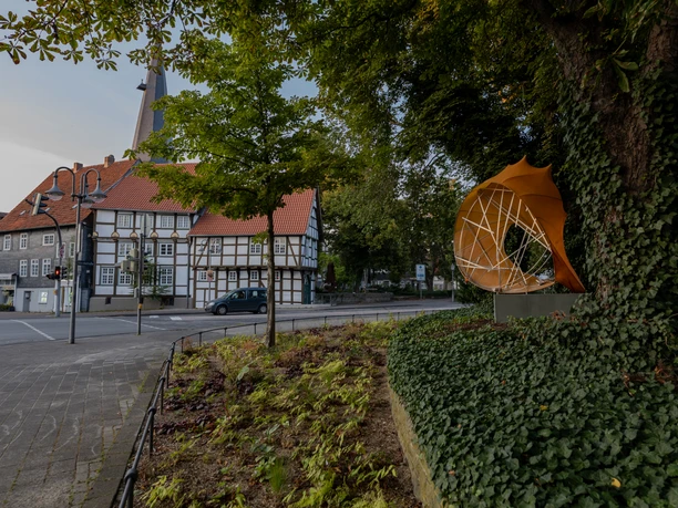 Gütersloh - blaue Stunde Fachwerkhäuser an einer ruhigen Straßenecke, umgeben von Bäumen und einer modernen Skulptur.