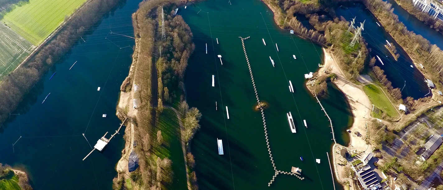 Anlage Wasserski-Langenfeld von oben mitsamt Campingplatz Wasserski-Anlage mit Seilbahnen auf Seen, umgeben von Bäumen; Campingplatz oben im Bild sichtbar.