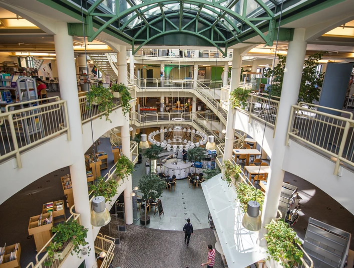 Stadtbibliothek Gütersloh Heller, moderner Innenraum eines mehrstöckigen Gebäudes mit Glasdach und begrünten Balkonen.