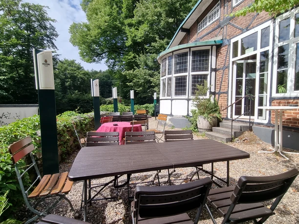 Terrasse Ein gemütlicher Außenbereich eines Cafés mit Holztischen und -stühlen, umgeben von grüner Natur.