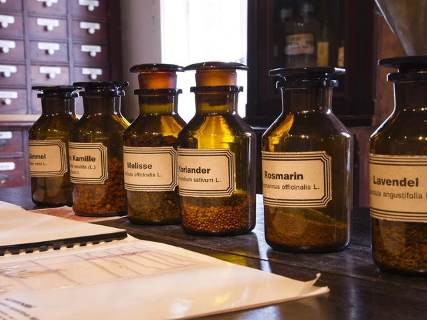 Apothekergläser mit getrockneten Kräutern wie Rosmarin und Lavendel auf einem Holztresen in einer alten Apotheke.
