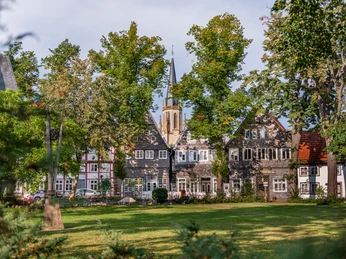 Kirchring-GT Historische Fachwerkhäuser und eine Kirche mit Turm inmitten grüner Bäume und einer gepflegten Rasenfläche.