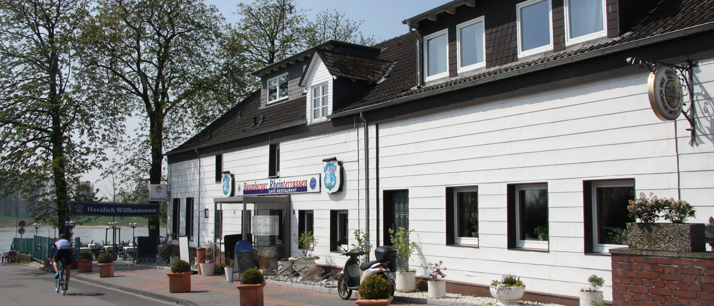 Baumberger Rheinterrassen in Monheim Baumberger Rheinterrassen in Monheim mit historischer Fassade und Außenterrasse am Flussufer.