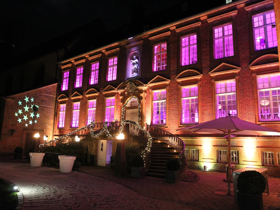 Alte Abtei im Lichterglanz von der Klosterpforte.jpg Historisches Gebäude bei Nacht mit violett beleuchteten Fenstern und festlich geschmücktem Eingang.