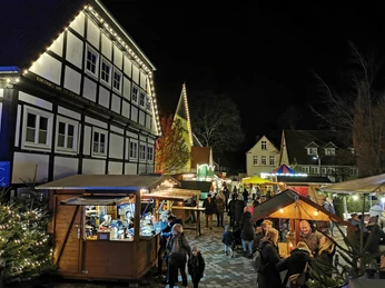 Adventsmarkt Nachtszene auf einem belebten Weihnachtsmarkt mit Fachwerkhaus, bunten Ständen und Besuchern.