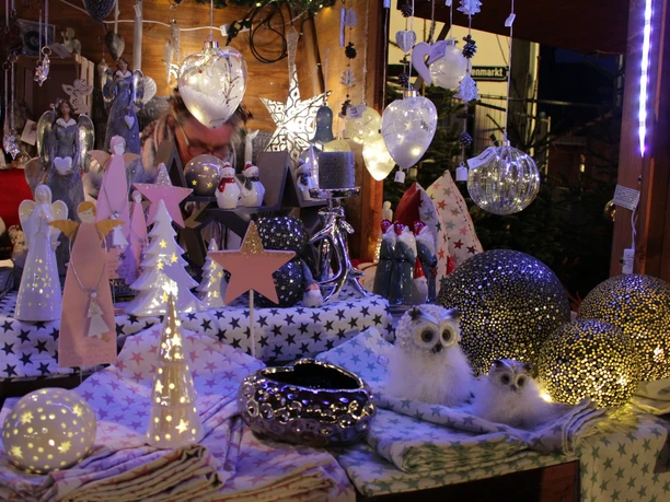 Ein festlich dekorierter Weihnachtsmarktstand mit beleuchteten Engeln, Sternen und Eulenfiguren.