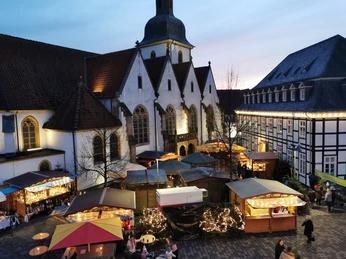 Adventsmarkt Weihnachtsmarkt mit festlich beleuchteten Ständen vor einer historischen Kirche in der Abenddämmerung.
