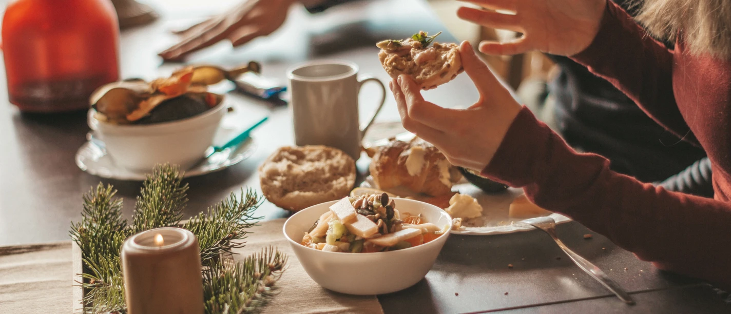 Zwei Personen frühstücken an einem Tisch mit Brötchen, einer Kerze, einem Früchtemüsli und Kaffee.