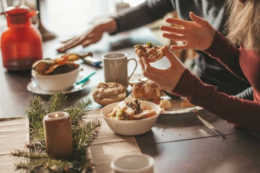Musterbild Frühstück Zwei Personen frühstücken an einem Tisch mit Brötchen, einer Kerze, einem Früchtemüsli und Kaffee.
