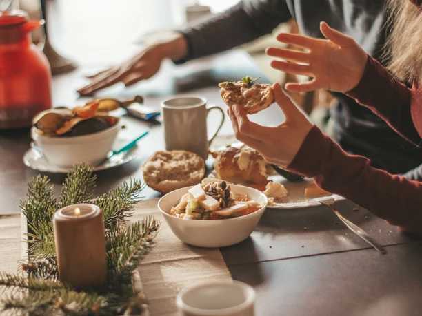 Musterbild Frühstück Zwei Personen frühstücken an einem Tisch mit Brötchen, einer Kerze, einem Früchtemüsli und Kaffee.