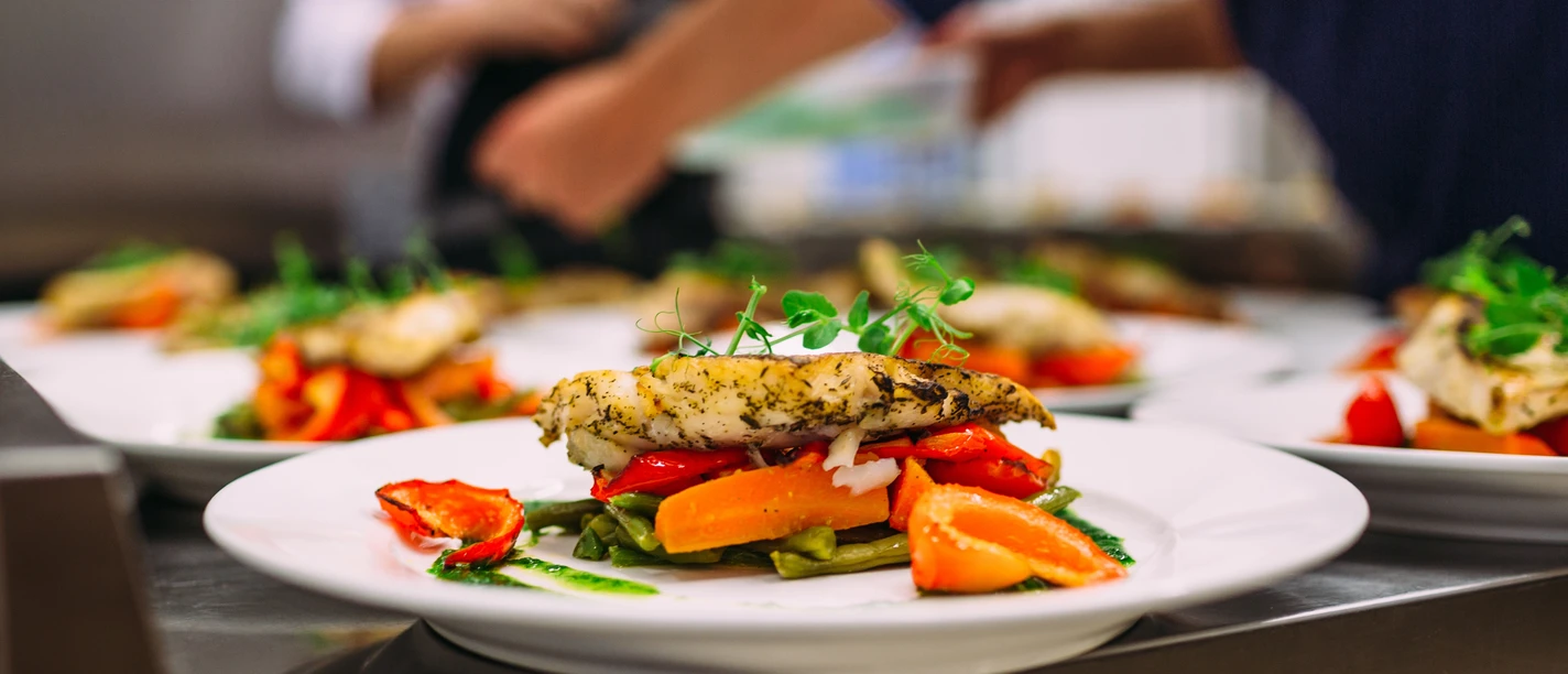 Musterbild Restaurant Ein kunstvoll angerichteter Teller mit gegrilltem Fisch, Gemüse und frischen Kräutern im Restaurant.