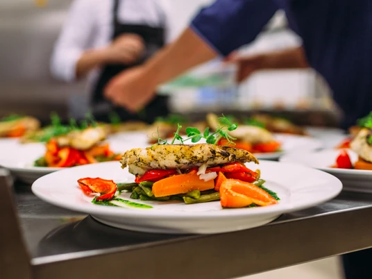 Musterbild Restaurant Ein kunstvoll angerichteter Teller mit gegrilltem Fisch, Gemüse und frischen Kräutern im Restaurant.