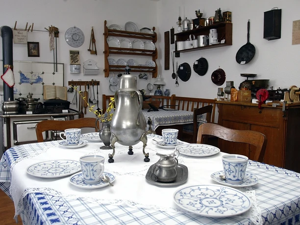 Bergische Kaffeetafel Historische Küche mit Esstisch, bemaltem Geschirr, silberner Kaffeekanne und traditionellem Ofen.